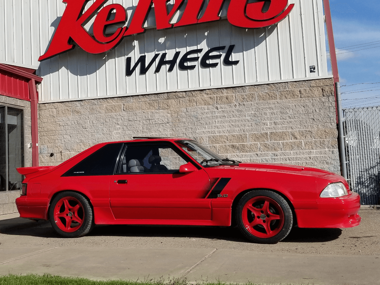 Red Mustang with custom wheels below Kelvins Wheel logo